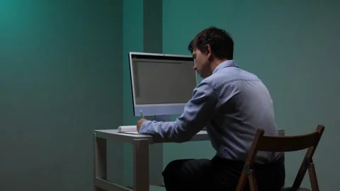 Man sitting at a desk, concentrating on a computer screen and writing notes on Stock Footage 345530013