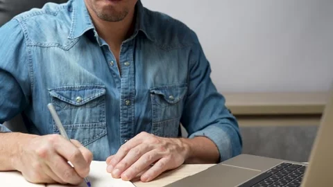 Man sitting at desk with laptop computer, writing something on notebook Stock Footage 254011317
