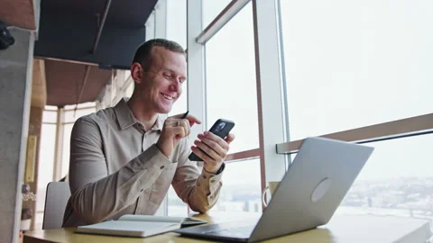 Man sitting at the desk, looking at his phone, talking and smiling  Stock Footage 174740170