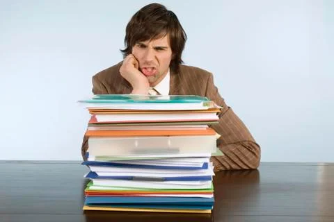 Man sitting on desk with stack of files, hand on chin 스톡 사진