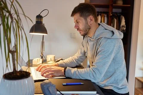 Man sitting at desk using laptop computer under desk lamp in home interior Stock Photos