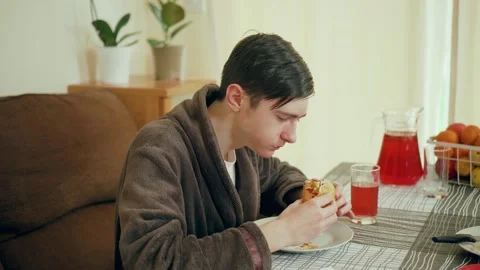 Man sitting at dining table eating hot dog. Male enjoying fast food meal while Stock Footage 306477680