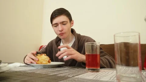 Man sitting at dining table eating hot dog and wiping mouth with napkin. Male Stock Footage 306478546