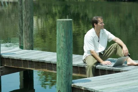 Man sitting on dock, using laptop computer, looking away Stock Photos