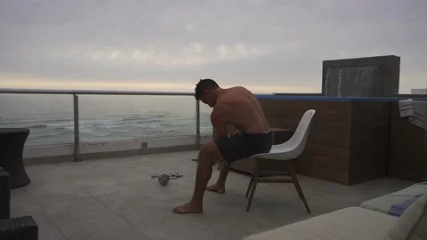 A man sitting doing biceps curl exercises with dumbbells on the terrace of a Vidéo 186210366