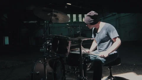 Man sitting down at drums and starting to play in dark warehouse Stock Footage 275103191