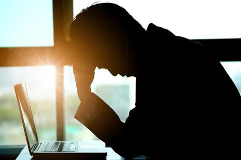 A man sitting down, his face unsettled. At the computer desk He has headaches Stock Photos
