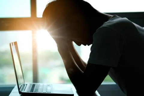 A man sitting down, his face unsettled. At the computer desk He has headaches Foto stock
