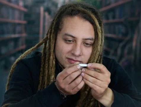 Man sitting down holding small joint between fingers staring at it, drug 스톡 사진