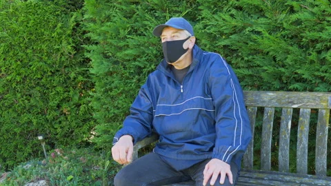 Man sitting down on a park bench, wearing a face mask. Vídeos de archivo 135597040