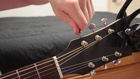 Man sitting down tuning the D string on his guitar Stock Footage 279909213