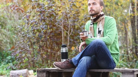 Man sitting, drinks tea or coffee and enjoy nature beauty, close thermos, autumn Видео 102889858