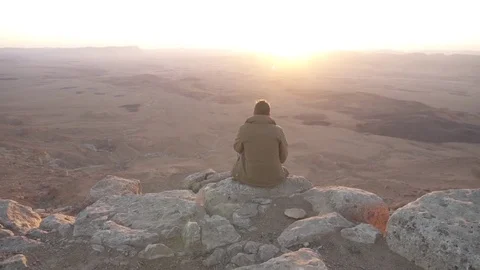 Man sitting on the edge of a desert mountain overlooking a sunrise Stock Footage 73080506
