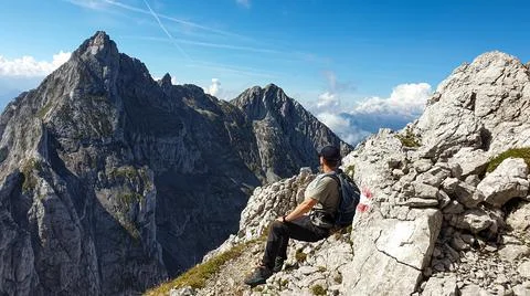 A man sitting at the edge of a mountain with a view on a vast valley Stock Photos