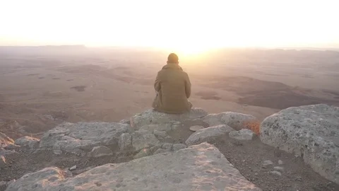 Man sitting on the edge of a mountain watching the desert sunrise Stock Footage 73080598