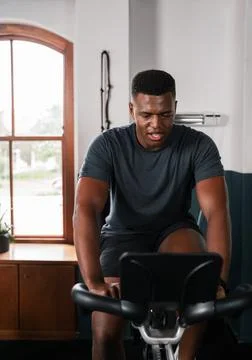 A man is sitting on an exercise bike in front of a window Stock Illustration