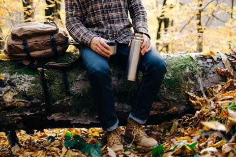 Man sitting on fallen tree trunk with thermos. Stock Photos