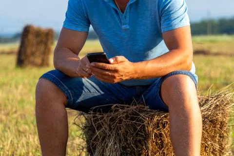 A man sitting in a field with a phone on a haystack. Foto stock