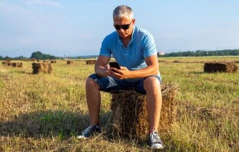 A man sitting in a field with a phone on a haystack. Foto stock
