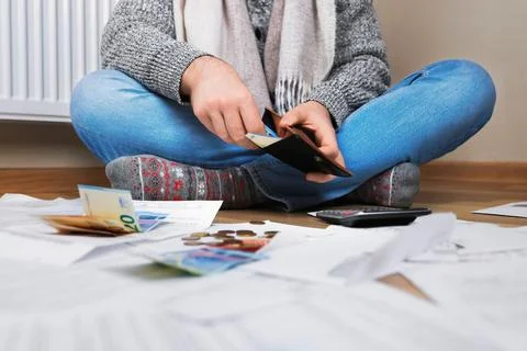 Man sitting on floor checking wallet near radiator surrounded by bills, eur.. Stock Photos
