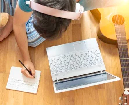 Man sitting on the floor learning to play the guitar. He his takes notes. Stock Photos