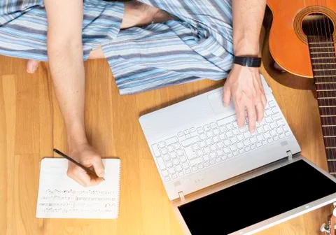Man sitting on the floor learning to play the guitar. He his takes notes. Stock Photos