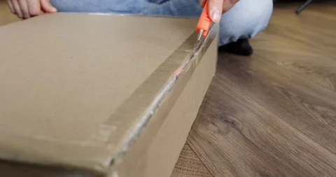 Man sitting on floor opens cardboard box with carving knife Stock Footage 286043592