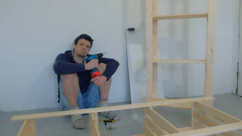 Man sitting on floor resting with electric screwdriver in hands collecting rack. Stock Footage 129592074