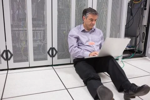 Man sitting on floor using laptop to check the servers Stock Photos