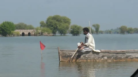 Man Sitting On Forward Bow Of Boat Slowly Rowing On Flood Waters With Stock Footage 241881834