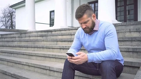 Man sitting in front of big house, browsing smartphone, steadicam shot 動画素材 74344981