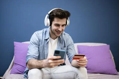 Man sitting in front of the computer holding a credit card at home - Young adult Foto stock