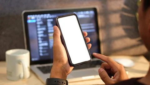 Man sitting in front of computer laptop and holding smart phone with white sc Stock Photos