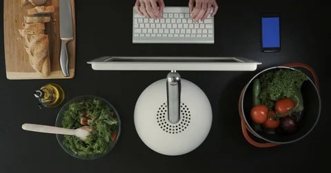 Man is sitting in front of his computer in the kitchen. Vegetables and bread are Stock Footage 76658742