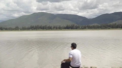 Man sitting in front of a lake and a mountain,meditating Video stock 273588873