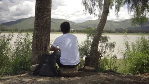 Man sitting in front of a lake and a mountain,meditating Stock Footage 273589170