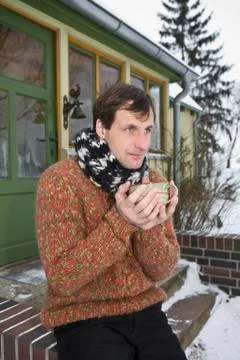 A man sitting on the front stoop of a house holding a hot drink Stock Photos