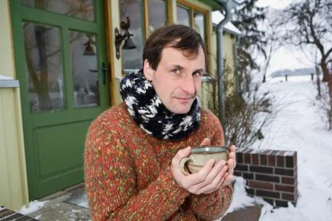 A man sitting on the front stoop of a house holding a hot drink Stock Photos