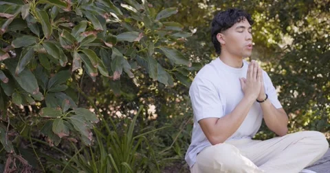 Man sitting on garden edge starting meditation to relax pressing hands breathing 動画素材 338168514