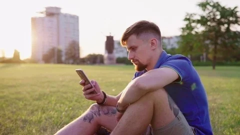 Man sitting on the grass and and flipping smartphone Stock Footage 78936946