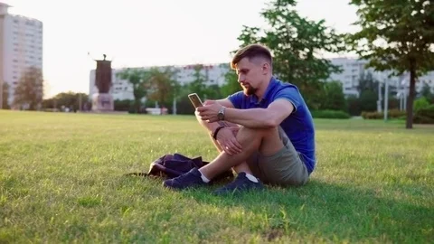 Man sitting on the grass and and flipping smartphone Stock Footage 78937292