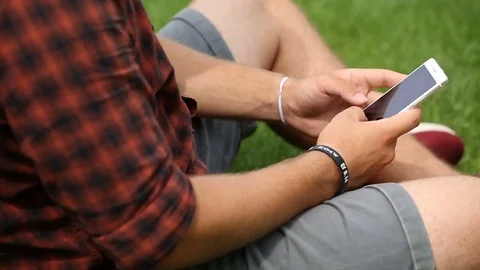 Man sitting on the grass and texting messages on smartphone Stock Footage 77474481