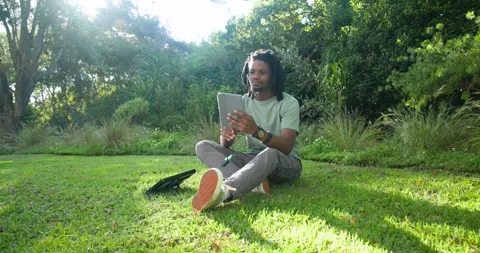 Man sitting on grass with backpack left, being prompted by tablet, checking Stock Footage 340965424