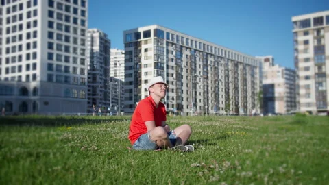 A man  sitting on the grass in the park on a background of the urban landscape Stock Footage 135652508