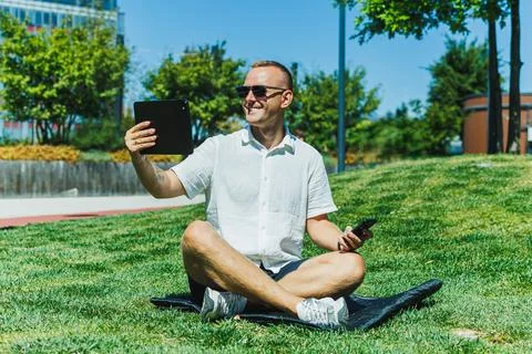 Man sitting on grass in a park using a tablet and smartphone on a sunny day Stock Photos