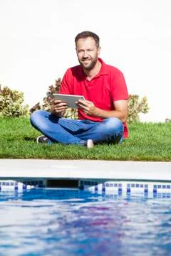 Man sitting on the grass, using a tablet. Stock Photos