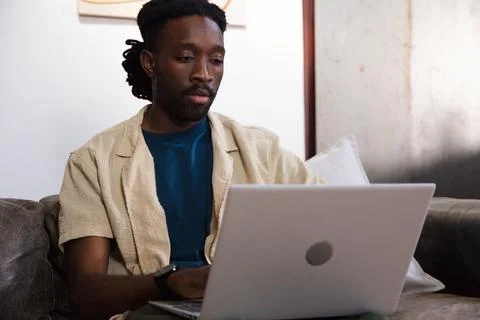 Man sitting on grey leather sofa working on silver laptop, wearing beige Stock Photos