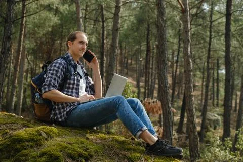 Man sitting on ground at forest talking on smartphone and working on laptop Stock Photos