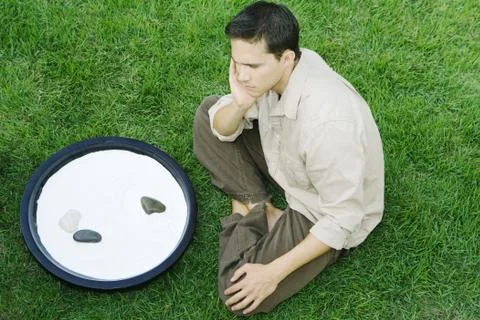 Man sitting on the ground next to rock garden, hand under chin, high angle view Fotos de archivo