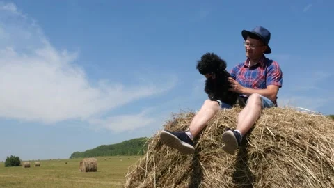 A man is sitting on a haystack with a dog. Stock Footage 135496669